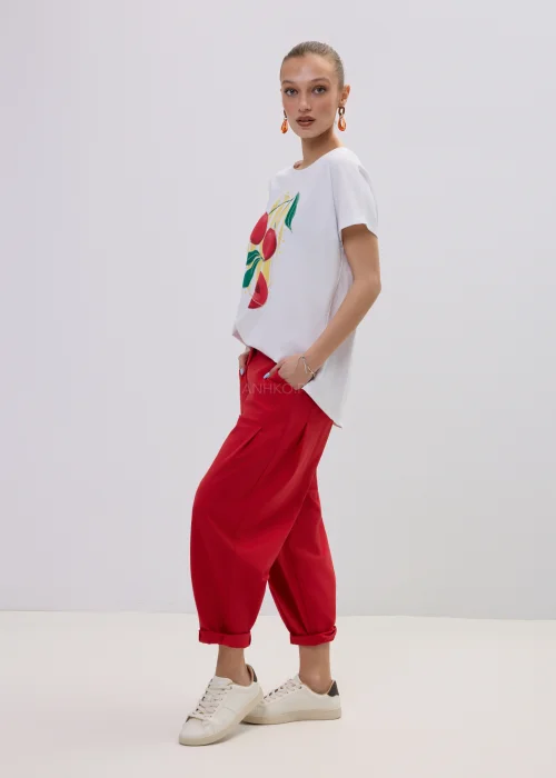 Biały t-shirt damski z kolorowym nadrukiem wiśni, luźny fason, zestawiony z czerwonymi spodniami.