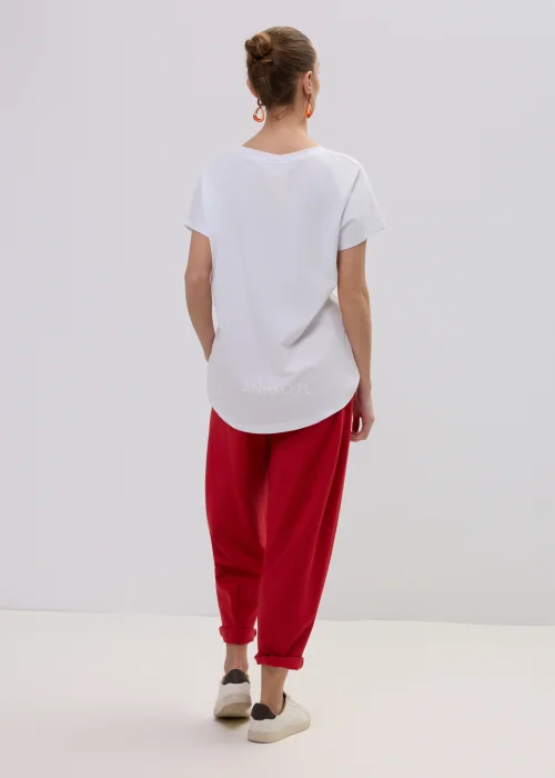 Biały t-shirt damski z kolorowym nadrukiem wiśni, luźny fason, zestawiony z czerwonymi spodniami.