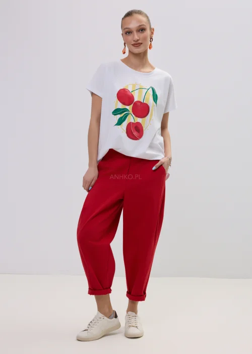 Biały t-shirt damski z kolorowym nadrukiem wiśni, luźny fason, zestawiony z czerwonymi spodniami.