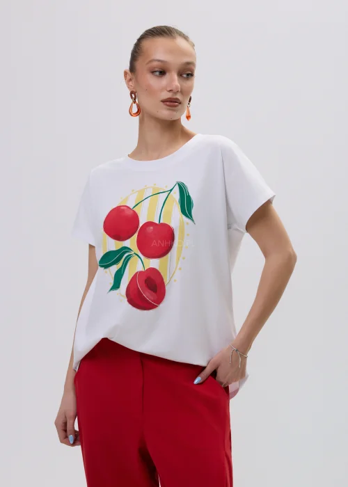 Biały t-shirt damski z kolorowym nadrukiem wiśni, luźny fason, zestawiony z czerwonymi spodniami.