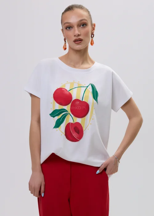 Biały t-shirt damski z kolorowym nadrukiem wiśni, luźny fason, zestawiony z czerwonymi spodniami.