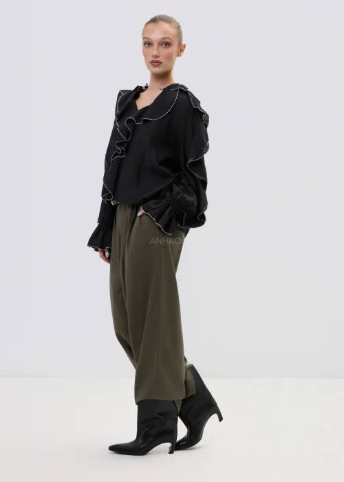 Czarna bluzka damska z falbanami i kontrastowym wykończeniem, luźny fason z długim rękawem, elegancka stylizacja ze spodniami w kolorze khaki.