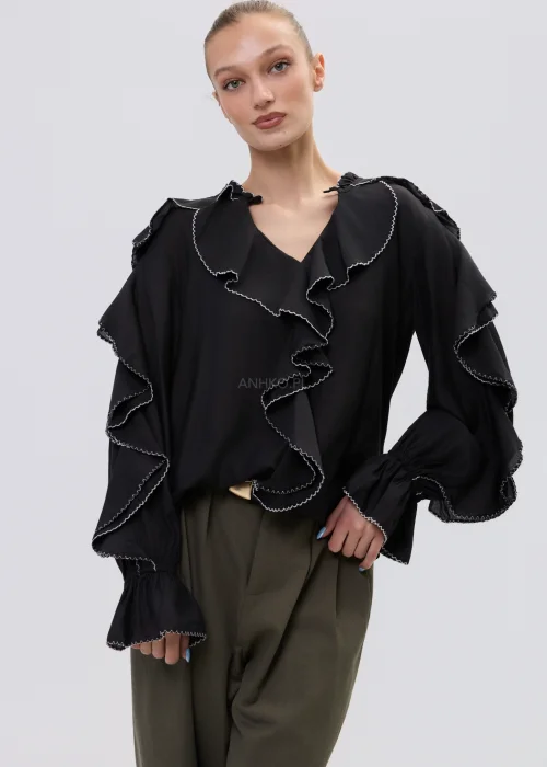 Czarna bluzka damska z falbanami i kontrastowym wykończeniem, luźny fason z długim rękawem, elegancka stylizacja ze spodniami w kolorze khaki.