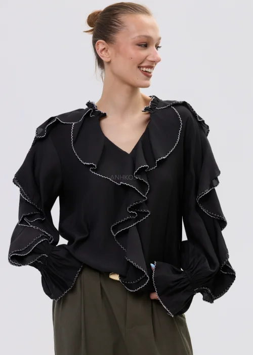 Czarna bluzka damska z falbanami i kontrastowym wykończeniem, luźny fason z długim rękawem, elegancka stylizacja ze spodniami w kolorze khaki.