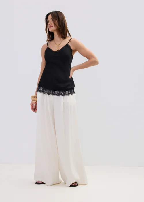 Czarna bluzka na ramiączkach z koronkowym wykończeniem przy dekolcie i dole, dopasowany fason, stylizacja z jasnymi spodniami.