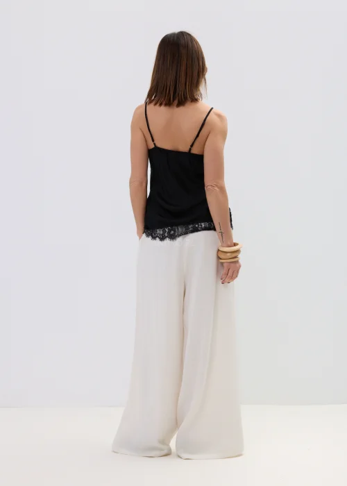 Czarna bluzka na ramiączkach z koronkowym wykończeniem przy dekolcie i dole, dopasowany fason, stylizacja z jasnymi spodniami.