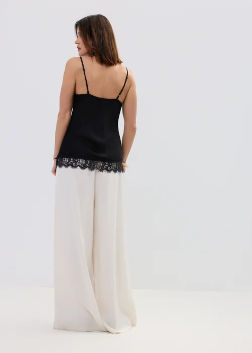 Czarna bluzka na ramiączkach z koronkowym wykończeniem przy dekolcie i dole, dopasowany fason, stylizacja z jasnymi spodniami.