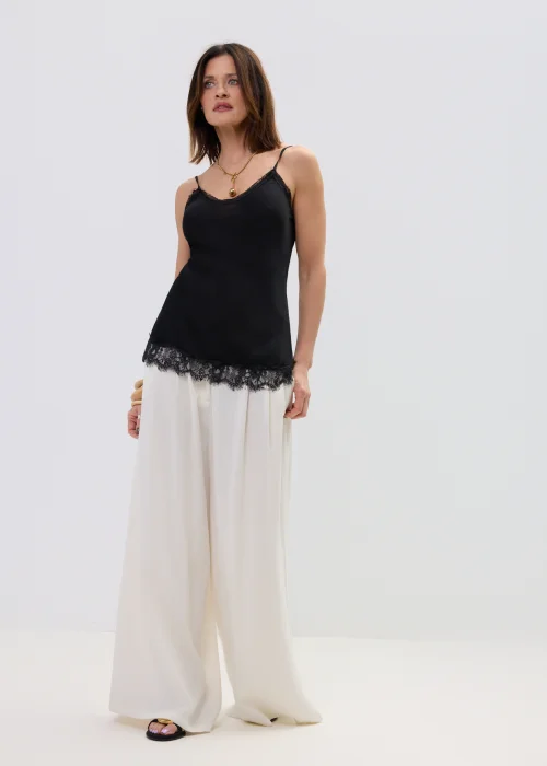 Czarna bluzka na ramiączkach z koronkowym wykończeniem przy dekolcie i dole, dopasowany fason, stylizacja z jasnymi spodniami.