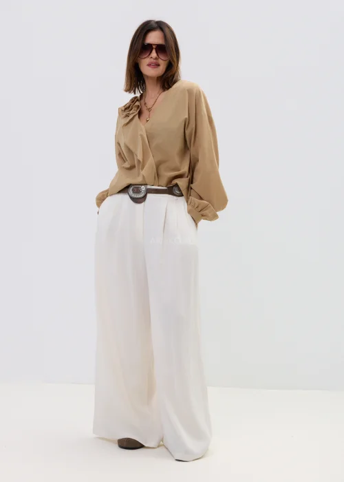 Camelowa bluzka damska z kopertowym dekoltem i falbaną, z długim rękawem, stylizowana z jasnymi spodniami i paskiem.