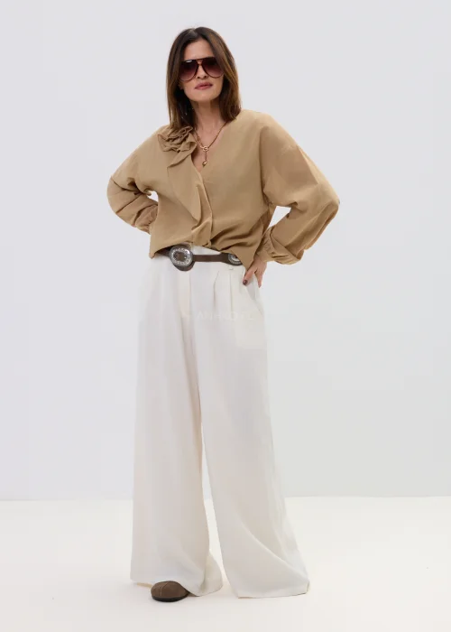 Camelowa bluzka damska z kopertowym dekoltem i falbaną, z długim rękawem, stylizowana z jasnymi spodniami i paskiem.