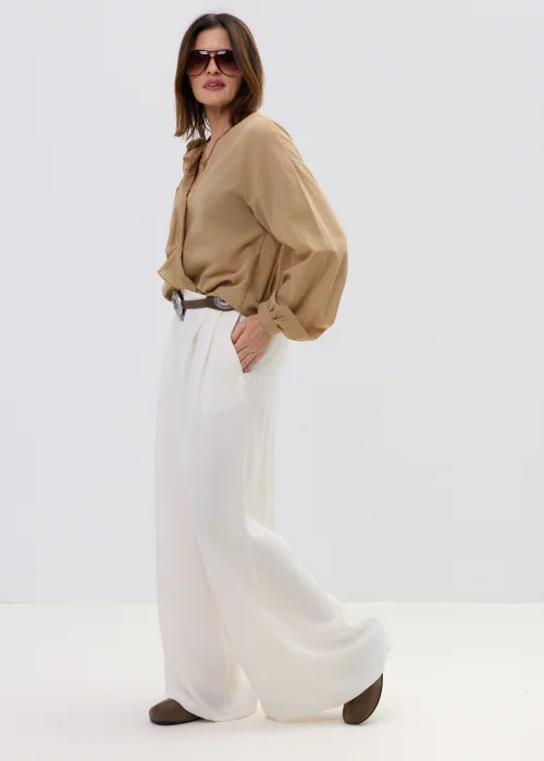 Camelowa bluzka damska z kopertowym dekoltem i falbaną, z długim rękawem, stylizowana z jasnymi spodniami i paskiem.