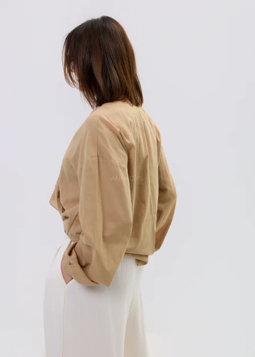 Camelowa bluzka damska z kopertowym dekoltem i falbaną, z długim rękawem, stylizowana z jasnymi spodniami i paskiem.