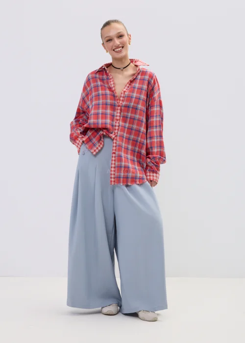 Koszula oversize w czerwono-niebieską kratę z postrzępionym wykończeniem, luźny fason z kołnierzem i guzikami, stylizacja casual z szerokimi spodniami.