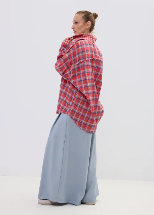 Koszula oversize w czerwono-niebieską kratę z postrzępionym wykończeniem, luźny fason z kołnierzem i guzikami, stylizacja casual z szerokimi spodniami.