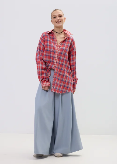 Koszula oversize w czerwono-niebieską kratę z postrzępionym wykończeniem, luźny fason z kołnierzem i guzikami, stylizacja casual z szerokimi spodniami.