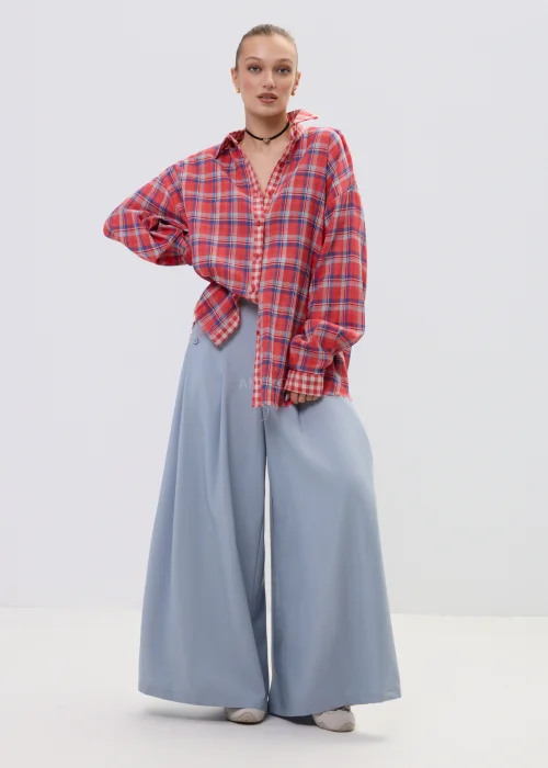 Koszula oversize w czerwono-niebieską kratę z postrzępionym wykończeniem, luźny fason z kołnierzem i guzikami, stylizacja casual z szerokimi spodniami.
