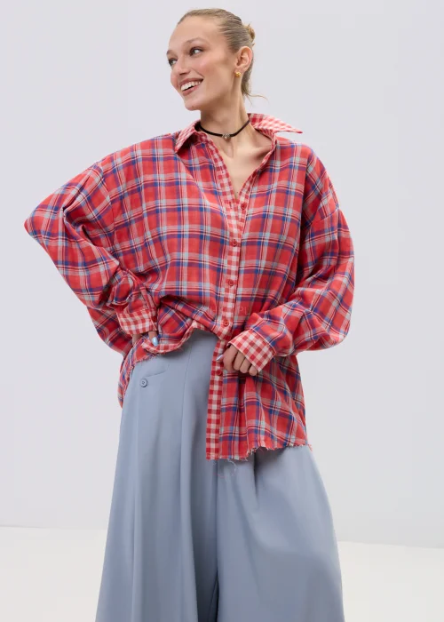 Koszula oversize w czerwono-niebieską kratę z postrzępionym wykończeniem, luźny fason z kołnierzem i guzikami, stylizacja casual z szerokimi spodniami.