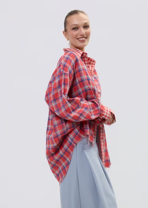 Koszula oversize w czerwono-niebieską kratę z postrzępionym wykończeniem, luźny fason z kołnierzem i guzikami, stylizacja casual z szerokimi spodniami.