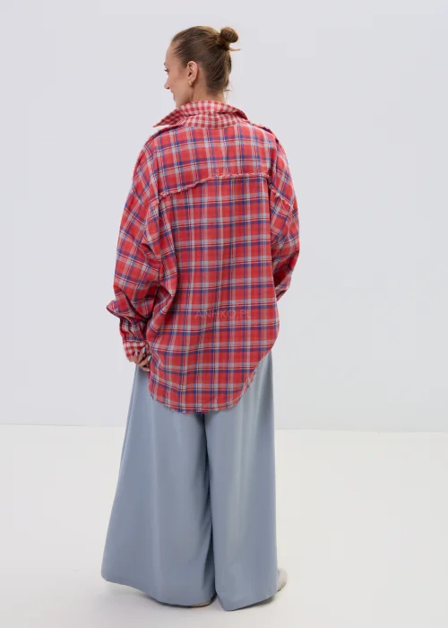 Koszula oversize w czerwono-niebieską kratę z postrzępionym wykończeniem, luźny fason z kołnierzem i guzikami, stylizacja casual z szerokimi spodniami.