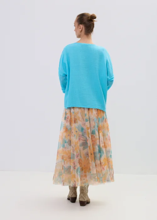 Turkusowa bluzka lniana damska o luźnym kroju z dekoltem V i ażurowymi rękawami, lekka i przewiewna, stylizacja ze zwiewną spódnicą w kwiaty.