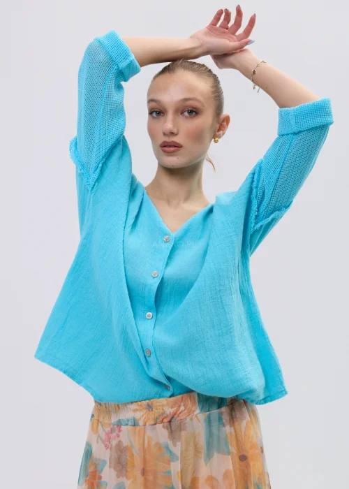 Turkusowa bluzka lniana damska o luźnym kroju z dekoltem V i ażurowymi rękawami, lekka i przewiewna, stylizacja ze zwiewną spódnicą w kwiaty.