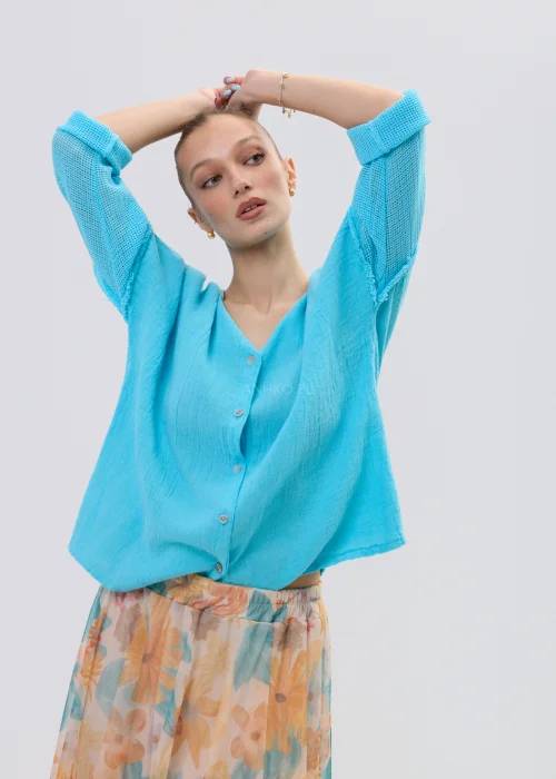 Turkusowa bluzka lniana damska o luźnym kroju z dekoltem V i ażurowymi rękawami, lekka i przewiewna, stylizacja ze zwiewną spódnicą w kwiaty.