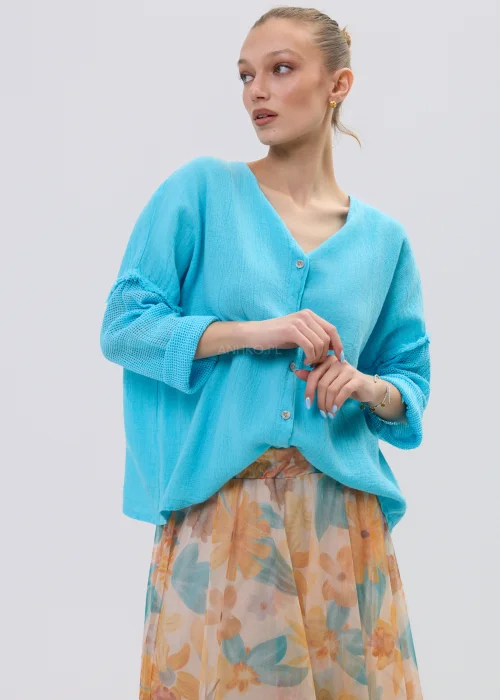 Turkusowa bluzka lniana damska o luźnym kroju z dekoltem V i ażurowymi rękawami, lekka i przewiewna, stylizacja ze zwiewną spódnicą w kwiaty.