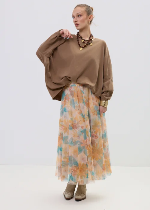 Brązowa bluzka oversize z długim rękawem o luźnym kroju, zestawiona z lekką spódnicą w pastelowy kwiatowy wzór.
