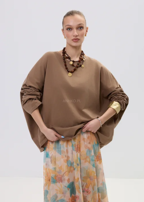 Brązowa bluzka oversize z długim rękawem o luźnym kroju, zestawiona z lekką spódnicą w pastelowy kwiatowy wzór.