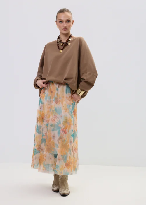 Brązowa bluzka oversize z długim rękawem o luźnym kroju, zestawiona z lekką spódnicą w pastelowy kwiatowy wzór.