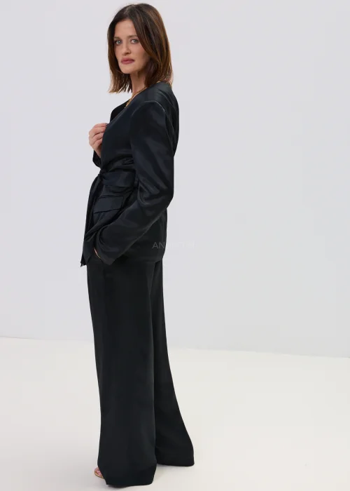 Czarny garnitur satynowy damski z wiązaną marynarką i szerokimi spodniami, elegancki zestaw o płynnej strukturze materiału.