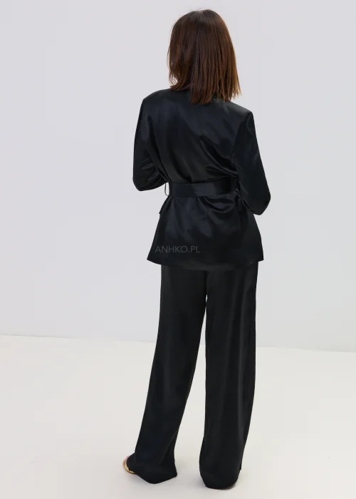 Czarny garnitur satynowy damski z wiązaną marynarką i szerokimi spodniami, elegancki zestaw o płynnej strukturze materiału.