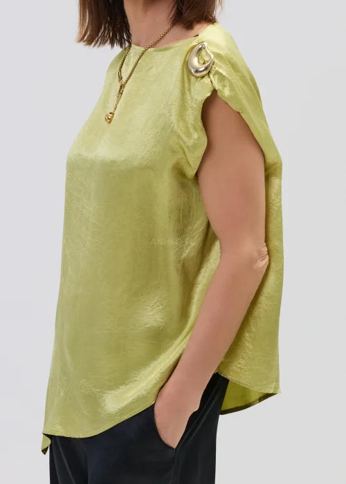 Limonkowa bluzka satynowa o luźnym fasonie z krótkim rękawem i ozdobnym pierścieniem na ramieniu, zestawiona z czarnymi spodniami, elegancka stylizacja.