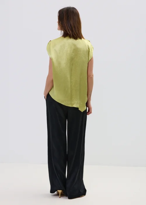 Limonkowa bluzka satynowa o luźnym fasonie z krótkim rękawem i ozdobnym pierścieniem na ramieniu, zestawiona z czarnymi spodniami, elegancka stylizacja.