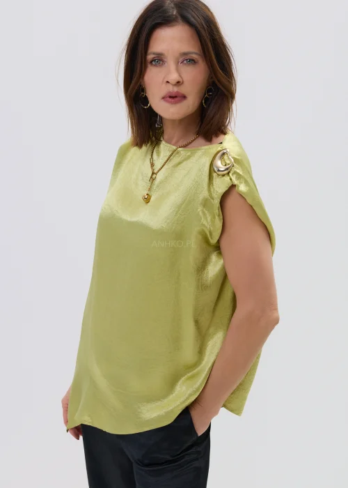 Limonkowa bluzka satynowa o luźnym fasonie z krótkim rękawem i ozdobnym pierścieniem na ramieniu, zestawiona z czarnymi spodniami, elegancka stylizacja.