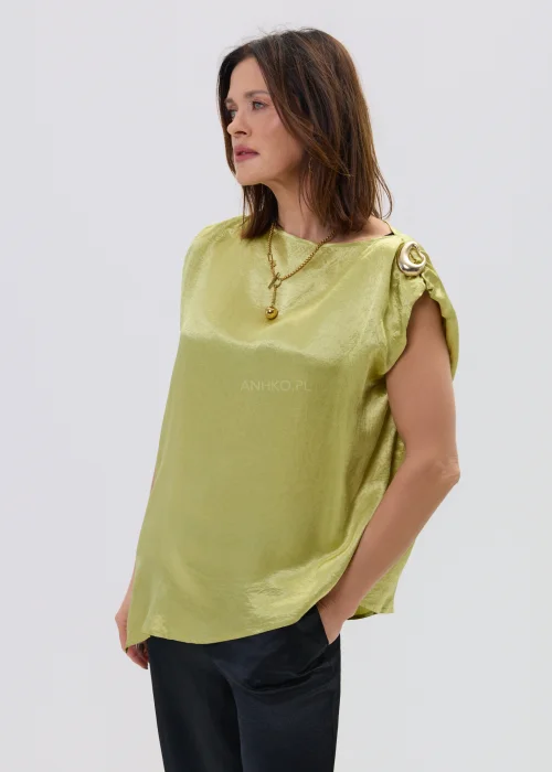 Limonkowa bluzka satynowa o luźnym fasonie z krótkim rękawem i ozdobnym pierścieniem na ramieniu, zestawiona z czarnymi spodniami, elegancka stylizacja.