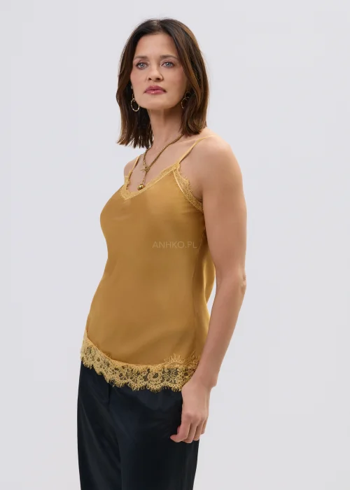 Miodowy top na ramiączkach z koronkowym wykończeniem przy dekolcie i dole, o lekkim, dopasowanym fasonie, zestawiony z czarnymi spodniami.
