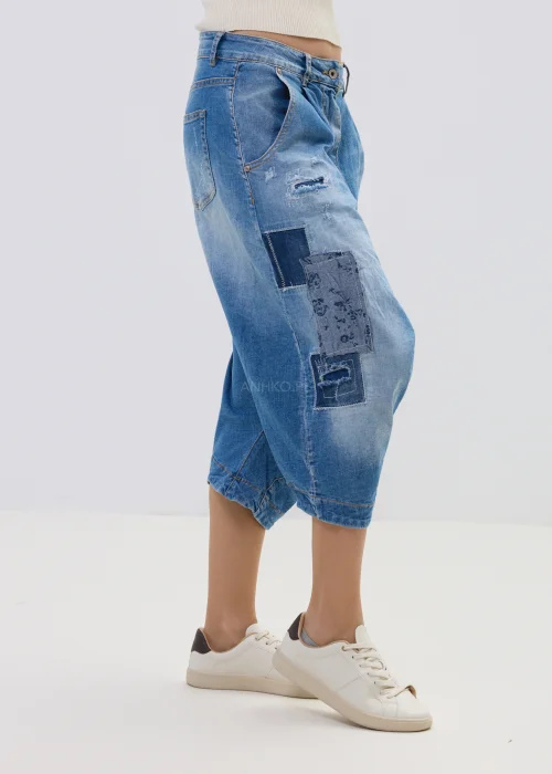 Jeansowe spodnie typu baggy z obniżonym krokiem i patchworkowymi wstawkami, w niebieskim odcieniu z przetarciami, zestawione z białymi sneakersami.