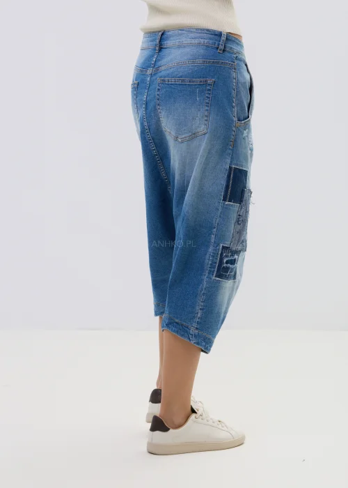 Jeansowe spodnie typu baggy z obniżonym krokiem i patchworkowymi wstawkami, w niebieskim odcieniu z przetarciami, zestawione z białymi sneakersami.
