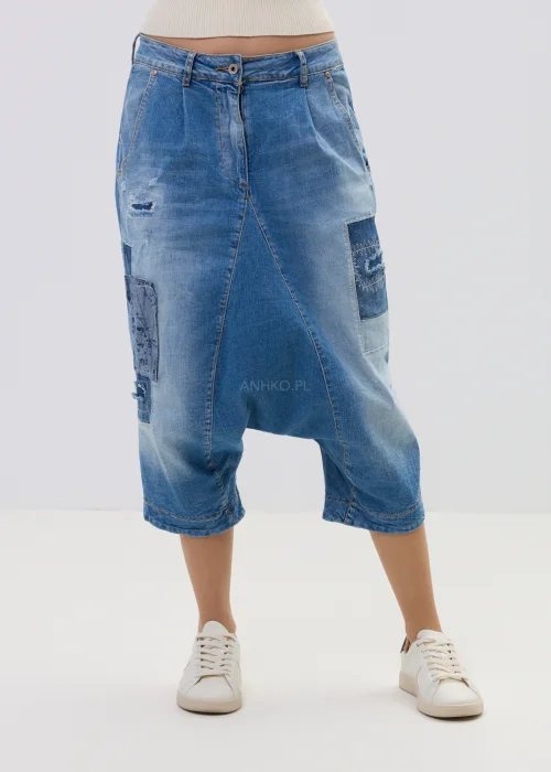 Jeansowe spodnie typu baggy z obniżonym krokiem i patchworkowymi wstawkami, w niebieskim odcieniu z przetarciami, zestawione z białymi sneakersami.