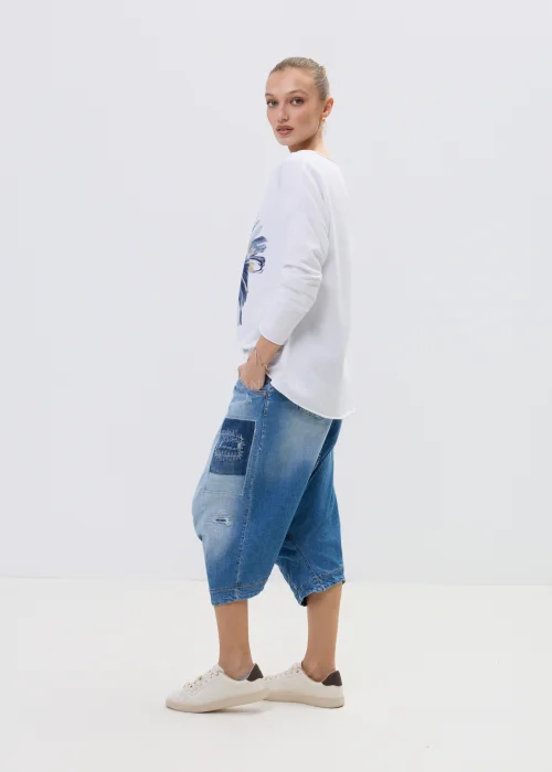 Jeansowe spodnie typu baggy z obniżonym krokiem i patchworkowymi wstawkami, w niebieskim odcieniu z przetarciami, zestawione z białymi sneakersami.