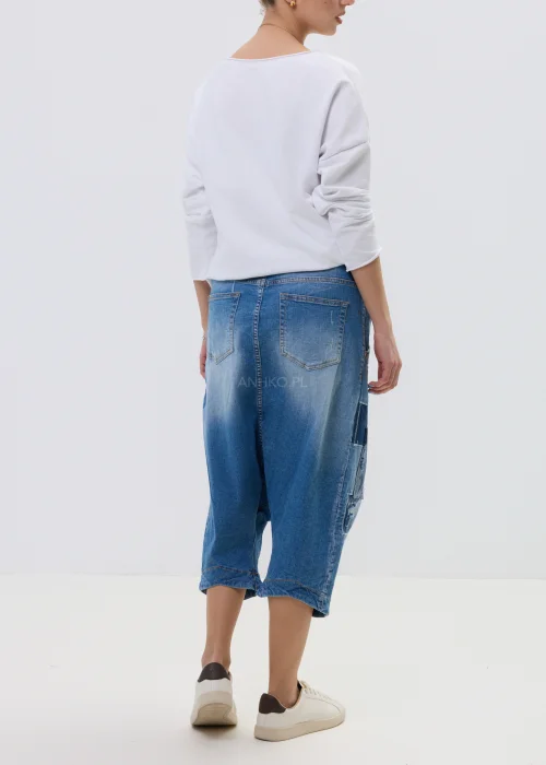 Jeansowe spodnie typu baggy z obniżonym krokiem i patchworkowymi wstawkami, w niebieskim odcieniu z przetarciami, zestawione z białymi sneakersami.