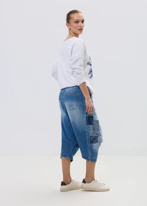 Jeansowe spodnie typu baggy z obniżonym krokiem i patchworkowymi wstawkami, w niebieskim odcieniu z przetarciami, zestawione z białymi sneakersami.