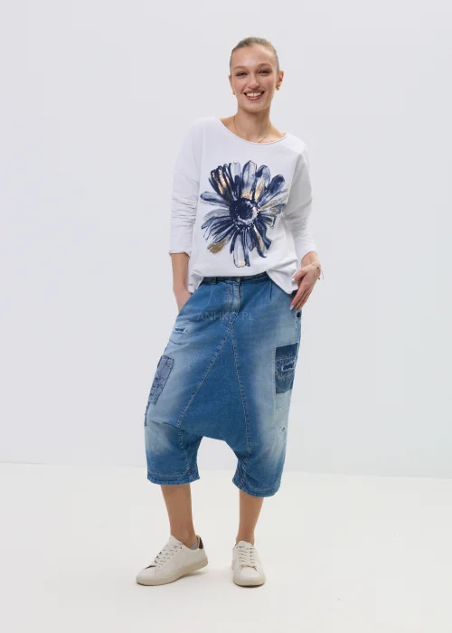 Jeansowe spodnie typu baggy z obniżonym krokiem i patchworkowymi wstawkami, w niebieskim odcieniu z przetarciami, zestawione z białymi sneakersami.