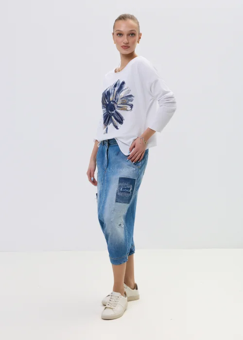 Jeansowe spodnie typu baggy z obniżonym krokiem i patchworkowymi wstawkami, w niebieskim odcieniu z przetarciami, zestawione z białymi sneakersami.