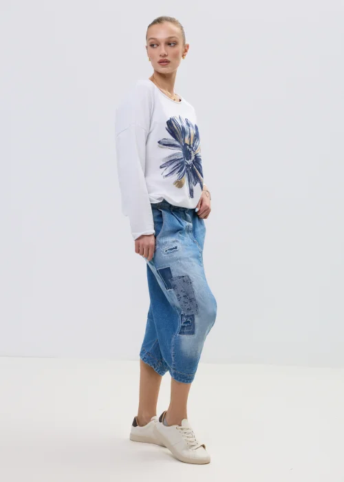 Jeansowe spodnie typu baggy z obniżonym krokiem i patchworkowymi wstawkami, w niebieskim odcieniu z przetarciami, zestawione z białymi sneakersami.