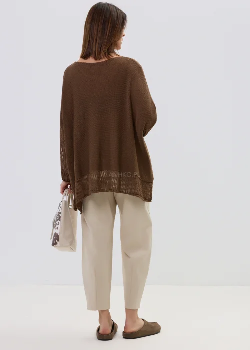 Brązowy sweter damski o luźnym, oversize’owym kroju z lekkiej dzianiny, zestawiony z jasnymi spodniami.