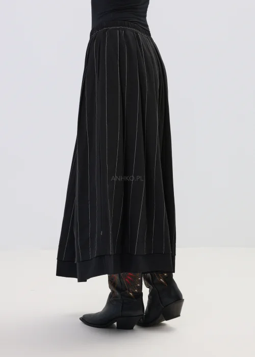 Czarna spódnica maxi z delikatnymi pionowymi prążkami, o rozkloszowanym fasonie i elastycznej talii, stylizowana z czarnymi botkami w stylu western.