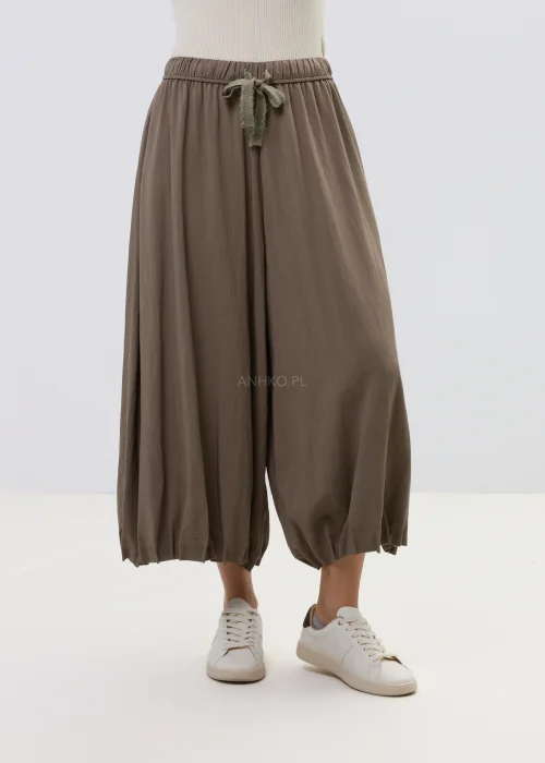 Brązowe spodnie damskie typu haremki z szerokimi nogawkami i gumką w pasie z wiązaniem, stylizowane ze sneakersami.