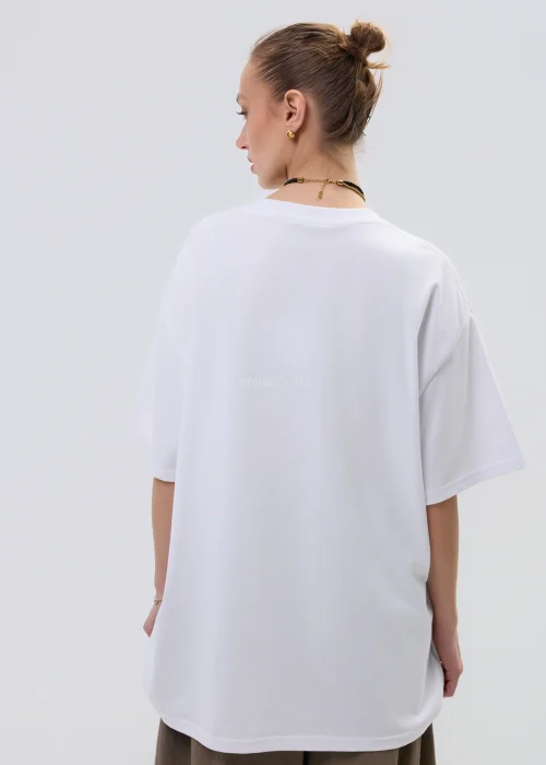 Biała bluzka oversize z dużą aplikacją dziewczynki w stylu cartoon z jeansową kokardą i zdobieniami, stylizowana ze spódnicą w casualowym looku.